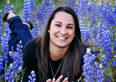 Senior girl posing laying down in a field of blue flowers smiling