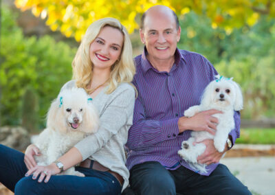 Man and woman sitting next to each other holding their two little white dogs