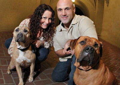 Man and woman squatting down behind their two large dogs