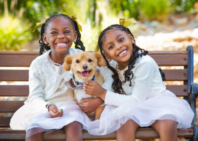 Two little girls sitting on a bench embracing their small dog in between them