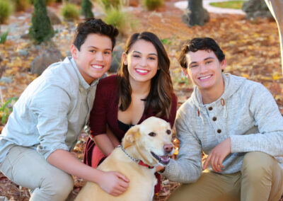 Young woman and two teen boys kneeling together embracing their dog for an outdoor session