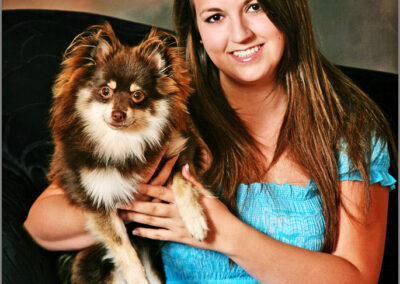 A young woman holding a Pomeranian dog on a black couch