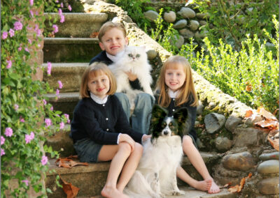 Three young children sitting on stone steps with their dog and cat