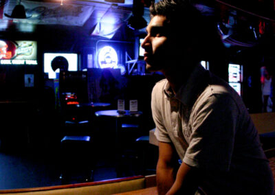 Young man posing leaning on a shuffle board underneath a bright bar light