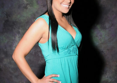 Senior girl smiling posing body to the side with one hand on hip against dark backdrop