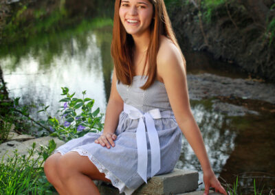 Senior girl smiling sitting on a rock wall with a creek in the background