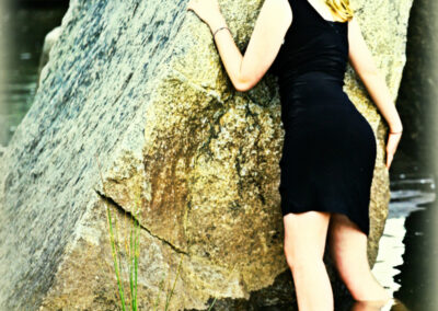 Senior girl standing in river water leaning against a large rock looking back over her shoulder