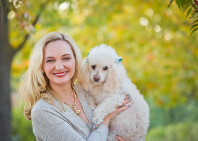 Woman outside in our portrait park in Citrus Heights, CA holding her white poodle with bows in its hair