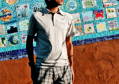 Senior boy posed standing looking off to the side behind a tiled wall mural