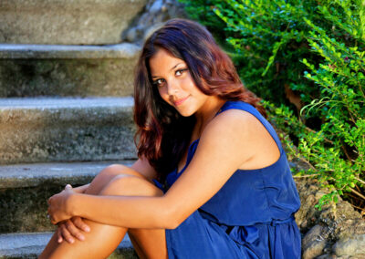 Senior girl sitting on steps body facing off to the side, head turned and smiling