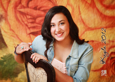 Senior girl sitting on chair, facing forward and smiling with orange backdrop