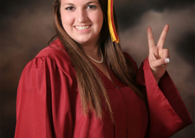 Senior girl posing with peace sign in Grad gown & cap with dark background