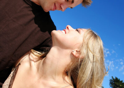 Couple at the beach with the blue sky in the background as they smile at each other lovingly