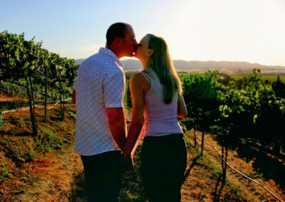 Couple posed in a kiss with backs to the camera while walking hand in hand down a vineyard. Engagement Session at RH Phillips Winery, CA