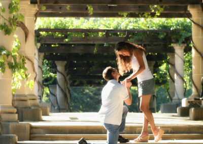 Engagement proposal pose under a wooden veranda with pillars wrapped in vines and greenery at Francis Ford Coppola Winery