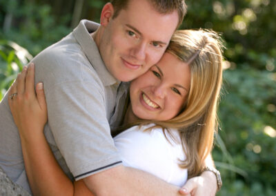 Couple in a loving embrace smiling facing the camera with outdoor greenery in the background