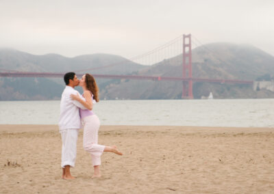 Couple posed kissing in a loving embrace on the beach with the Golden Gate Bridge in the background