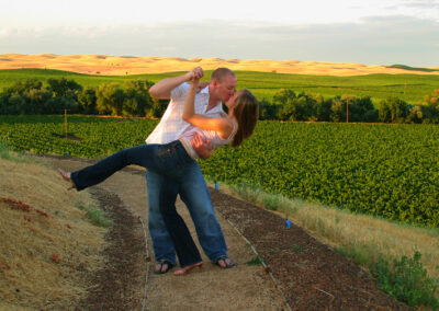 Couple in a loving embrace with wife dipped back into a kiss with beautiful green fields and hills in the background at RH Phillips Winery, CA