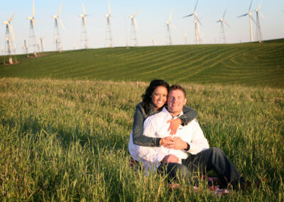 Couple lovingly embracing each other laying in the green fields with windmills in the background