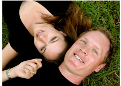 Couple laying together on the grass while looking up and smiling